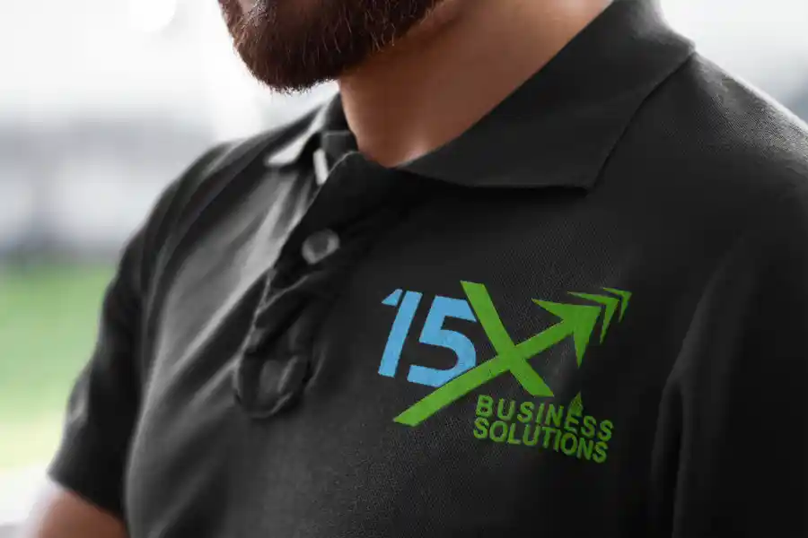 Close-up of a black polo shirt featuring the 15X Business Solutions logo.